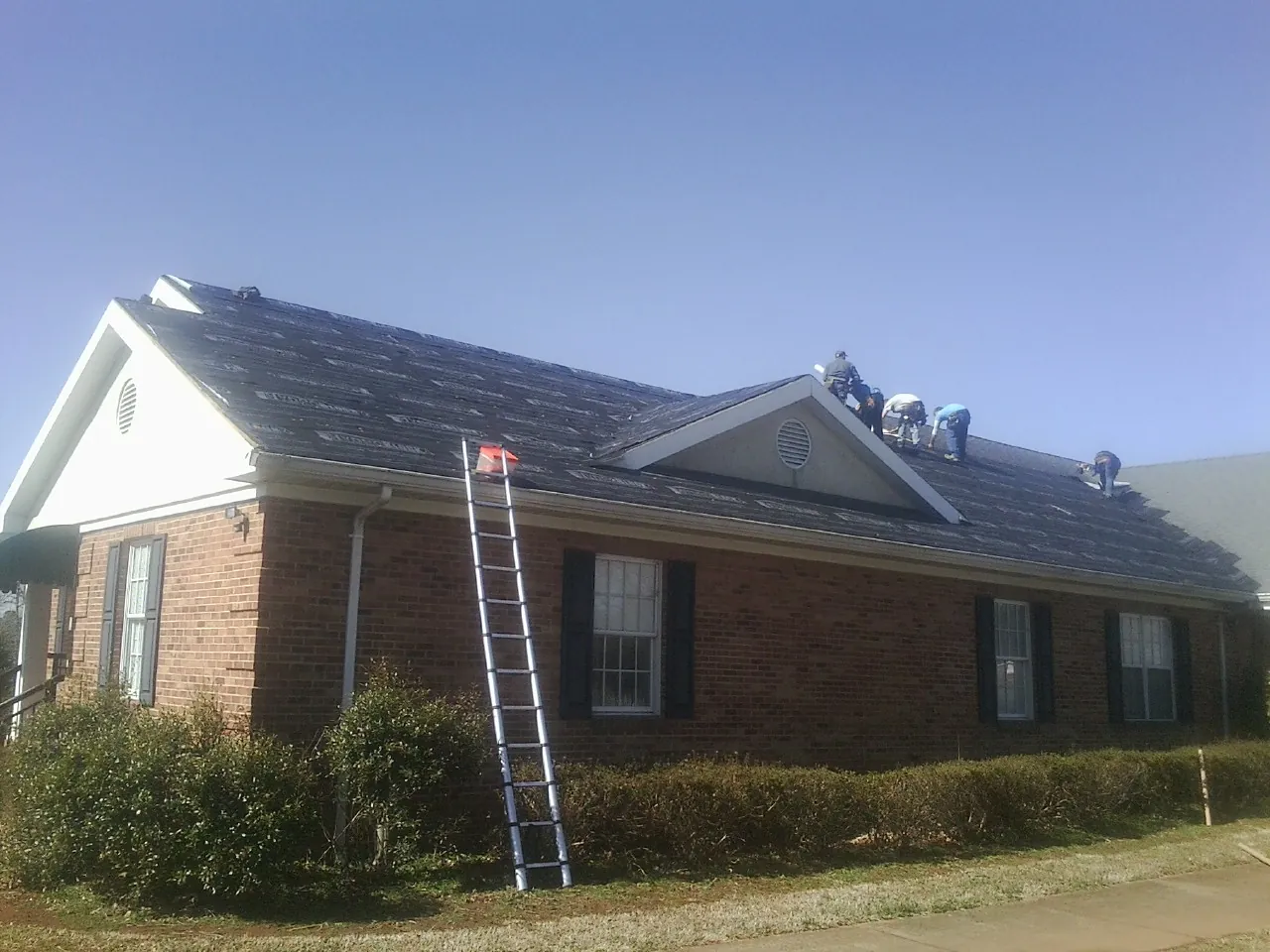 Crew tearing shingles off a brick ranch roof with a ladder set — Emergency Roof Repair work by our crew in Alsea