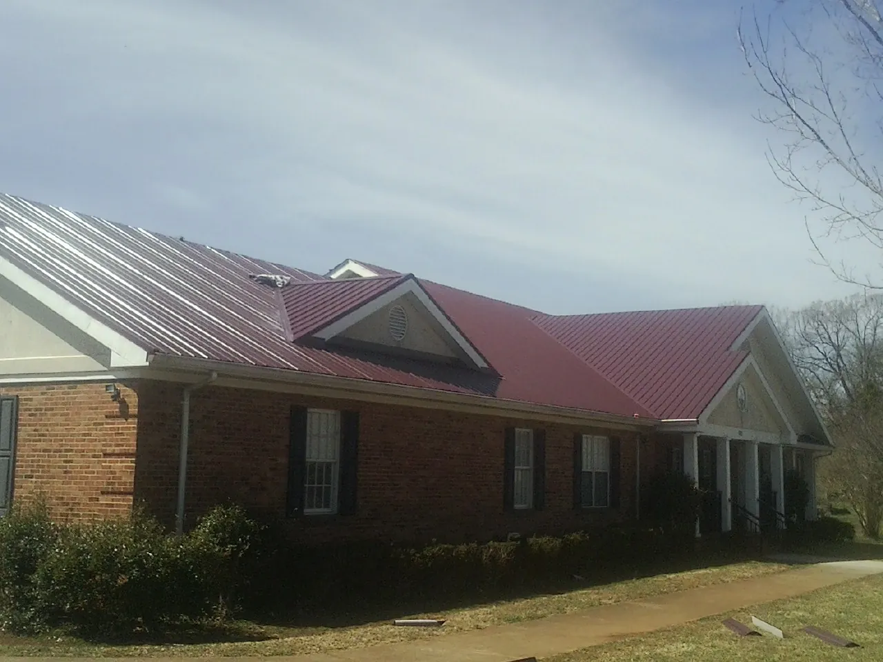 Red metal roof with gabled entries on a long brick building, from a Hail Damage Roof Repair job in Alsea