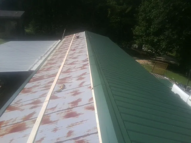 Old rusted panels beside newly installed green metal roofing — Wind Damage Roof Repair by Roofing Brothers in Alsea