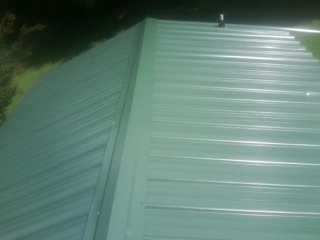 New green metal panels meeting at the ridge of a roof — Flat Roof Repair work by our crew in Alsea